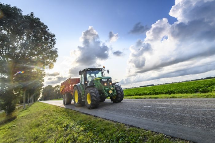 John Deere tractor hauling a tipper trailer on a country road in between agricultural fields