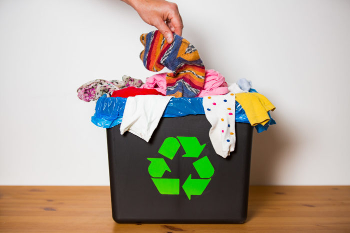 Hand putting used sock in bin with recycling sign.