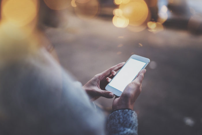 Woman holding hands smartphone in night atmospheric city.Female hands using mobile phone.Closeup on blurred background.Flares, bokeh effects.