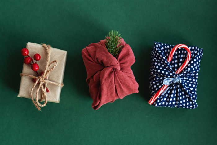 Christmas gifts wrapped in red textile with decor. Sustainable gifts. Zero waste. Xmas eco holiday. Traditional Japanese Furoshiki style. View from above. Flat lay