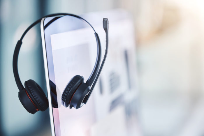 Closeup of headset hanging on a computer desktop monitor in an empty call centre office. Operating helpdesk for customer service and sales support. Telemarketing agents providing online assistance